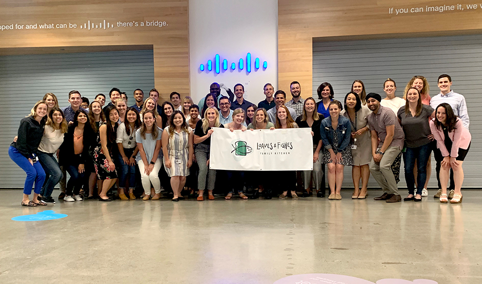 Large group of people pose and hold a sign that reads “Loaves & Fishes” with Cisco logo in the background.