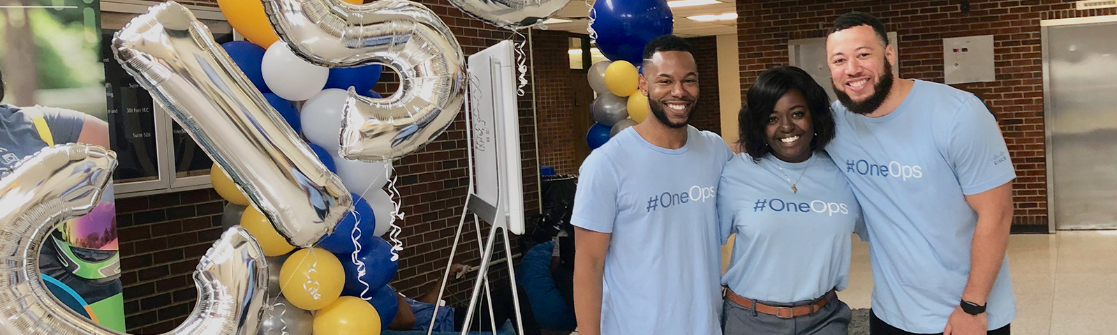 Three people stand together smiling and wearing shirts that read, “#OneOps.”