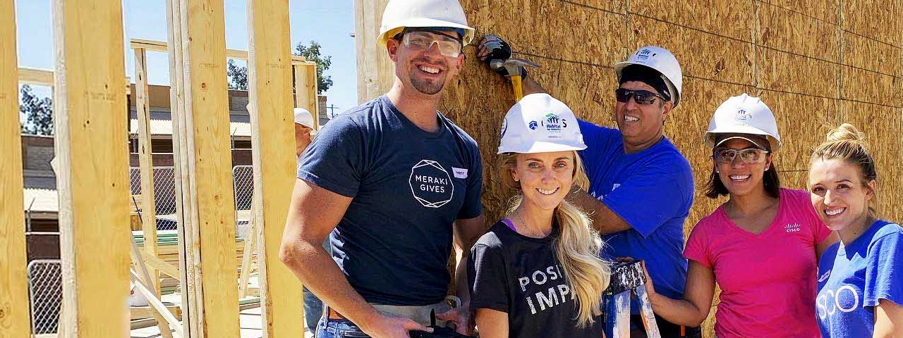 Five employees smiling wearing hard hats as they build a house for a team volunteer event